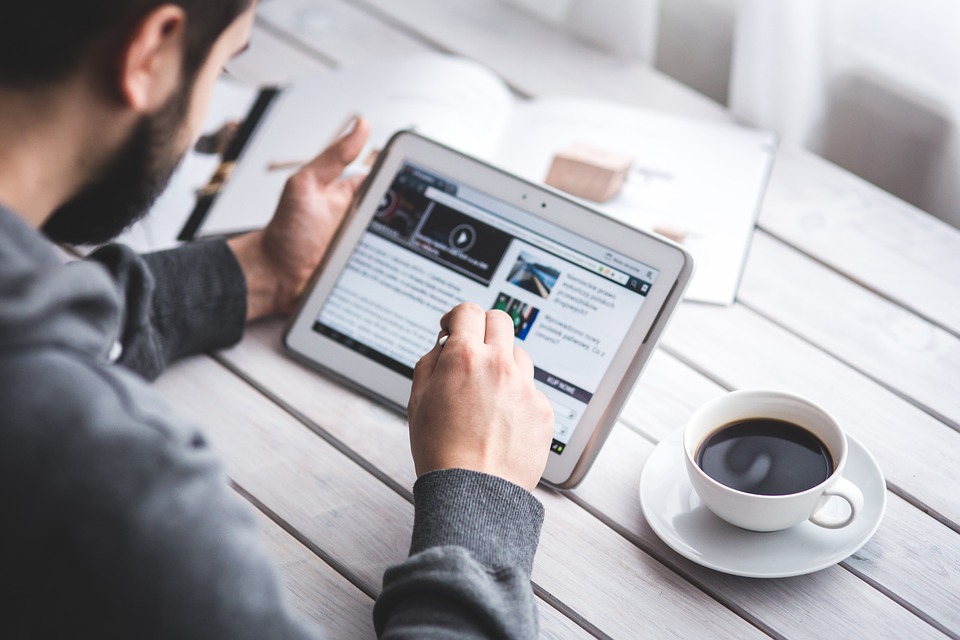 man looking at iPad with cup of coffee next to him